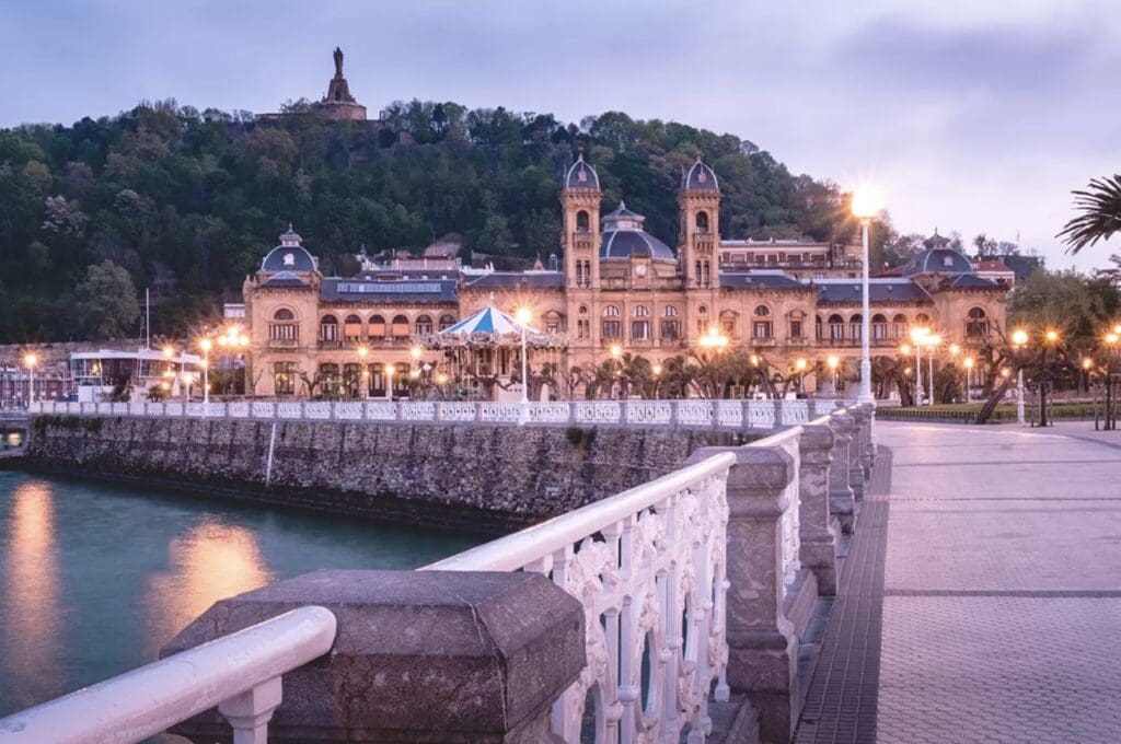 San Sebastián City Hall illuminated at dusk with Monte Urgull and the Christ statue rising above it, Basque Country, Spain