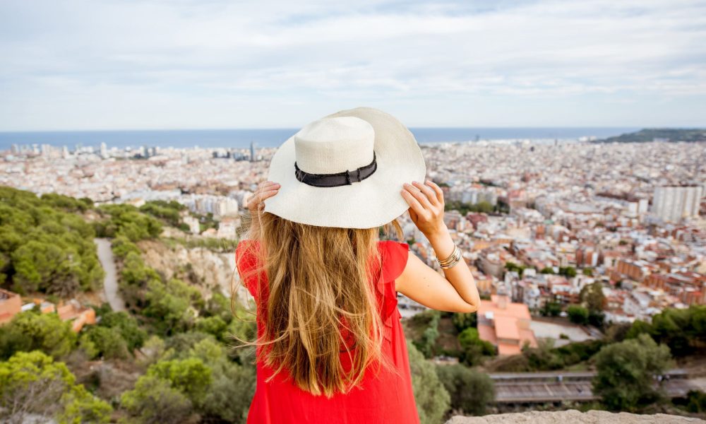 Young woman tourist in hat enjoying great cityscape view on Barcelona